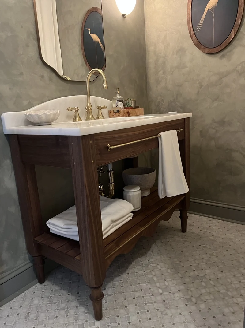 A green bathroom with a stone vanity, brass fittings and framed art.